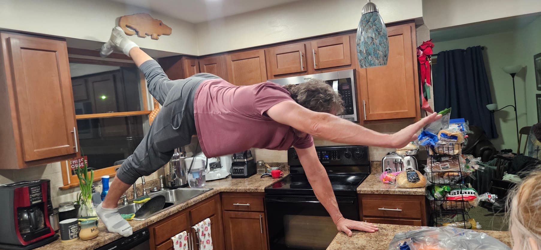 Tobe holding a plank across the kitchen counters with one foot in the air.