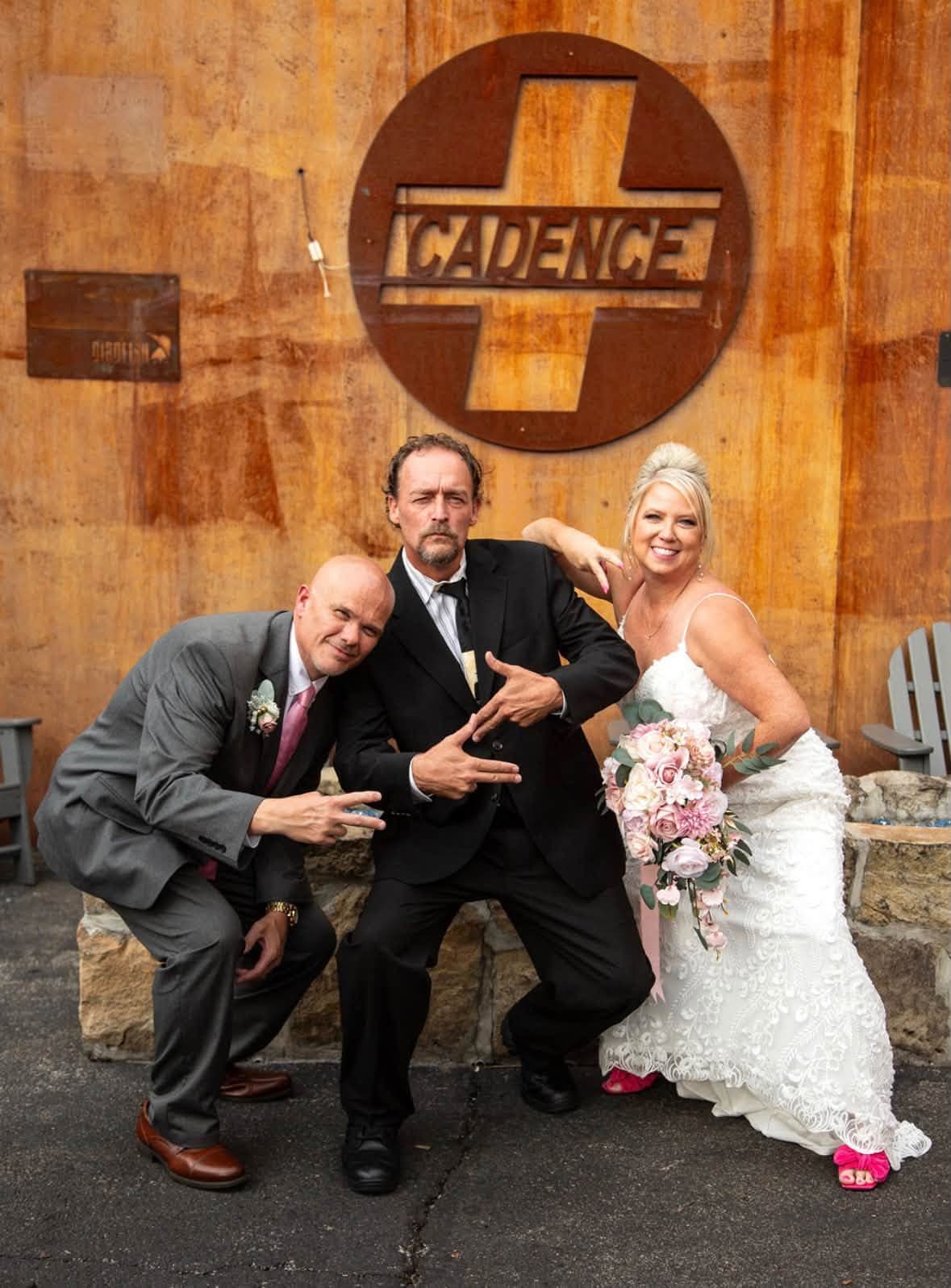 Tobe clowning for the camera with Michael and Cassandra on their wedding day, in front of a rusted Cadence sign.